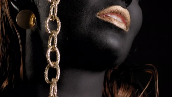 Closeup of a Woman with Black and Gold Paint and a Gold Chain Posing in Studio