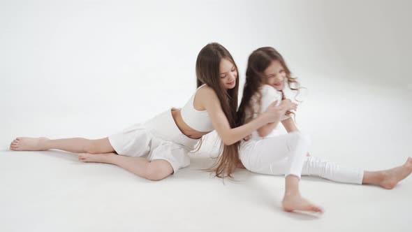 Little Girls with Long Hair in White Clothes Play Indulge and Tickle Each Other