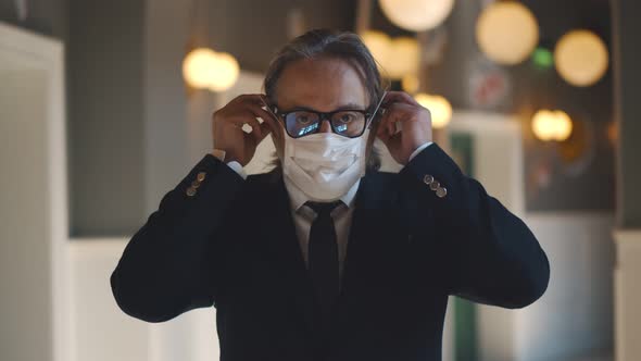 Portrait of Serious Mature Businessman Putting on Medical Mask