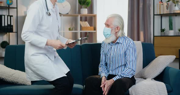 Doctor in Protective Mask Visiting Her Senior Male Patient and Attantivly Listening