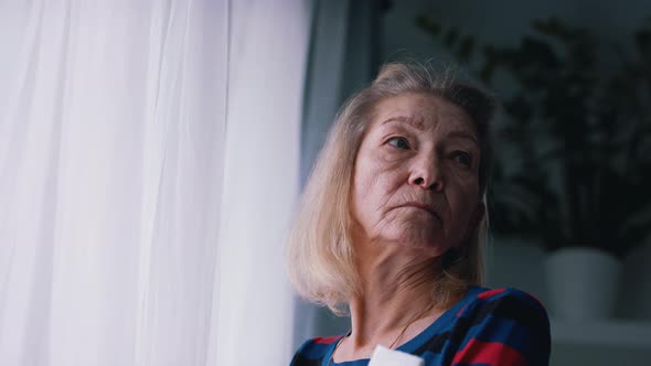 Pensive Old Woman Thinking Near the Big Window