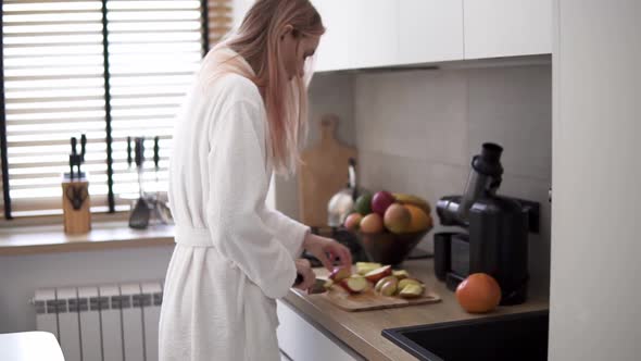 Woman at Kitchen Cutting Apple with a Knife on a Wooden Cutting Board to Make Juice