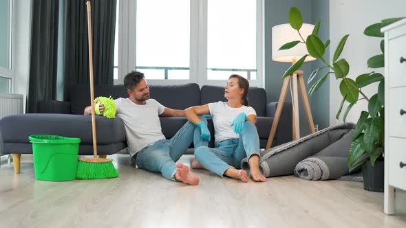 Tired Couple Sits on the Floor in a Room and High Five Each Other After They Finish Cleaning the