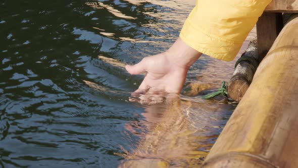 Female hand touching the water in lake while rafting a bamboo raft on a winter morning.