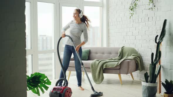 Beautiful Woman Is Hoovering the Floor at Home Using Modern Vacuum Cleaner and Listening To Music