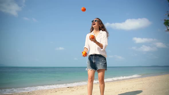 Young Cheerful Woman Juggles Tangerines on the Beach on a Sunny Day.