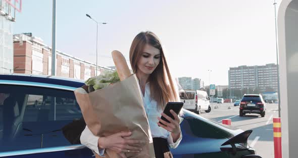 Woman With A Mobile Phone Near Recharging Electric Car