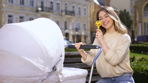 Smiling Female Entertaining Baby With Rattle Toy, Happy Young Mother in Park