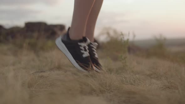 Women's athletic legs in black sneakers jump on rope in field. Closeup. Concept of healthy lifestyle