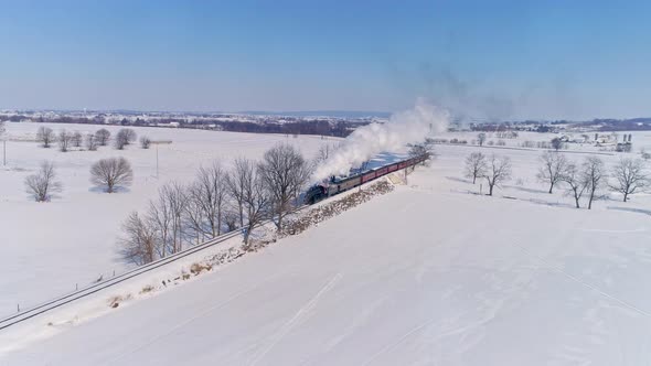 Aerial View of an Antique Steam Locomotive Approaching Pulling Passenger Cars and Blowing Smoke and Steam After a Snow Storm