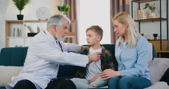 Doctor Checking Boy Patient's Heart Beat with Stethoscope and Talking to Boy's Mother