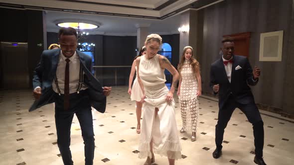 Carefree guests and newlyweds dancing in hall together