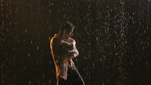 Young Attractive Man Dancing in the Rain in a Dark Studio. Wet Clothes Fit the Athletic Body