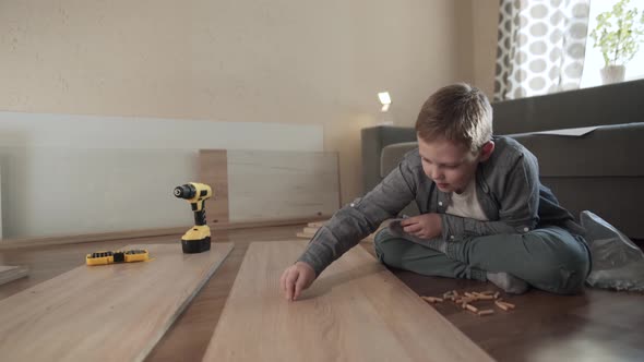 Caucasian Boy Sits on Floor and Inserts Wooden Dowels Into Chipboard Panel