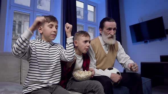 Senior Man and Two Teenage Boys which Watching on TV Football Match and Rejoicing