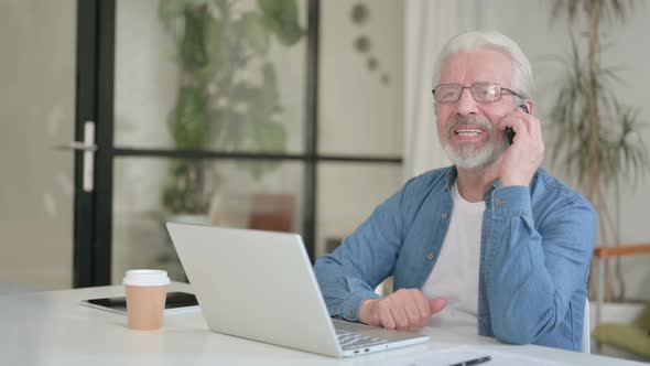 Senior Old Man Talking on Phone While Using Laptop