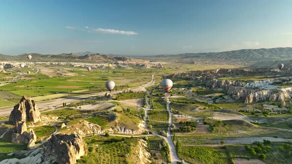 Hot air balloons fly over the mountainous landscape of Cappadocia, Turkey.