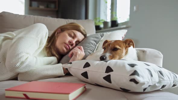 Woman Sleeps on Couch with Book and Dog Lying Near