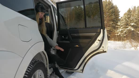 Young Woman Sitting in Car Cleaning Snow From Legs After Winter Walk in Park