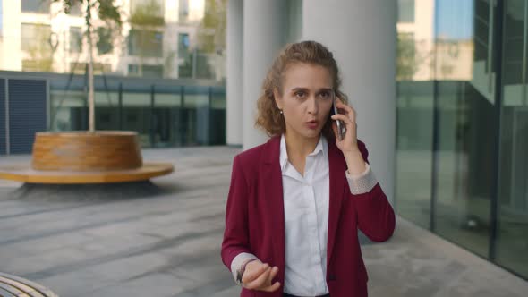 Young Worried Businesswoman Talking on Smartphone Walking Near Office Center Outdoors