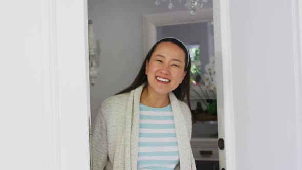 Happy asian woman opening front door, smiling and greeting visitor to home