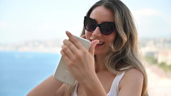 Caucasian smiling woman in sunglasses using smartphone with view of Nice on the background, France. 