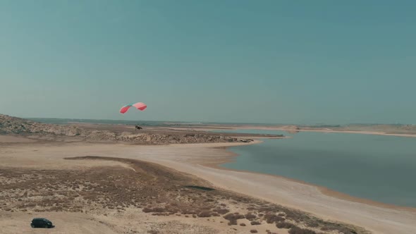 Aerial View Of Motorised Paraglider Flying Over Arid Coastline Next To Salt Lake. Follow Shot