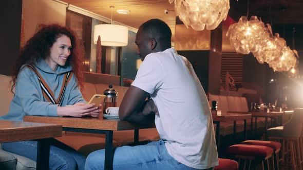 A Lady and an African Man are Chatting in a Cafe