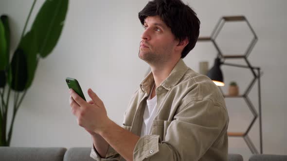 A Young Man Using a Smartphone Thinks and Looks Sideways