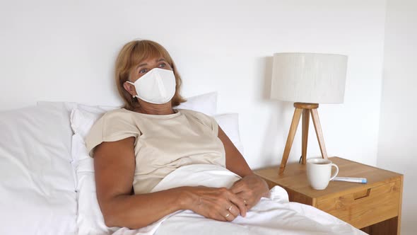 Ill Caucasian Woman in a Protective Face Mask Lying Down in Bed in Her Room Isolated to Prevent