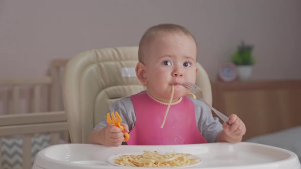 Toddler eats spaghetti for dinner by himself holding two forks