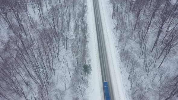 Aerial View of Truck Driving on a Road Surrounded By Winter Forest in Snowfall