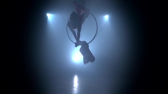 Gymnasts Performs a Trick in the Aerial Hoop. Black Smoke Background. Silhouette