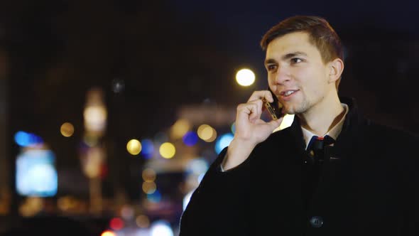 A Young Man Walks Through the Night City Uses a Smartphone