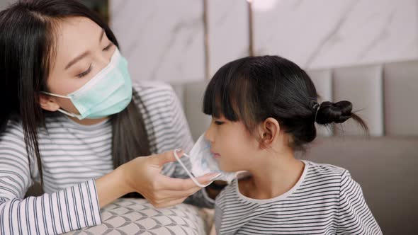 Asian young mother wearing face mask for  kid at home  prevent Covid 19 infection