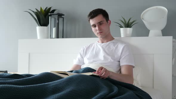 Young Man Reading Book while Sitting in Bed