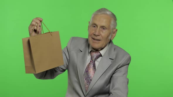 Elderly Man with Shopping Bag. Looks Into the Camera and Stretches the Gift