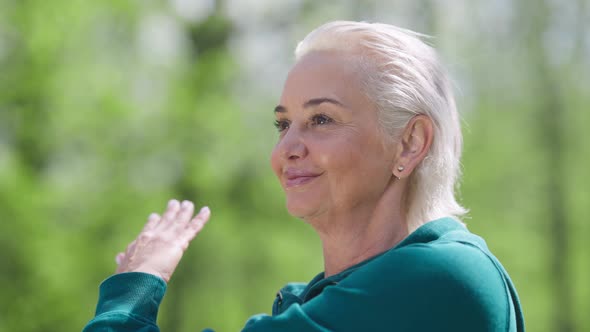 Closeup Portrait of Smiling Confident Fit Retiree Stretching Hand Muscles in Sunlight Outdoors