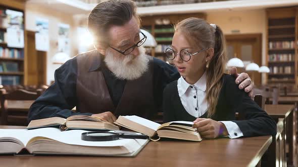 Happy Grandfather and Granddaughter Which Sitting in the Library and Reading Books Together