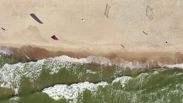 AERIAL: Top View Shot of Surfer Riding Waves Near Baltic Sea Shore with People Walking on a Beach