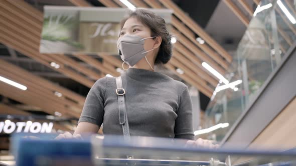 Young asian female wears face mask protection / shopping cart alone on escalator