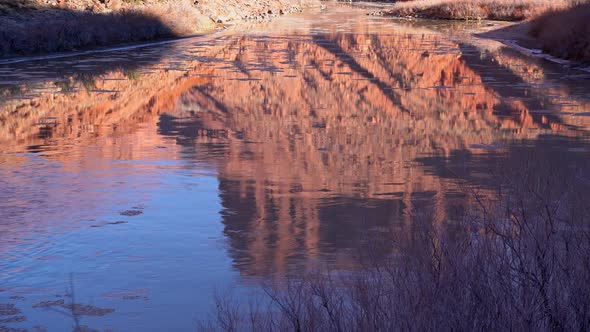 Colorado River reflecting red cliffs in Moab Utah with ice floating downstream