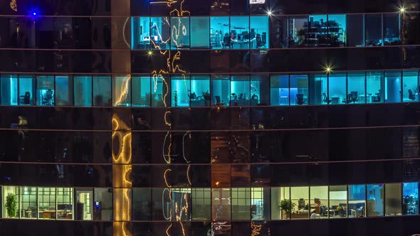 Office Windows of a Glazed Skyscraper Glow at Night with City Lights Reflection Aerial Timelapse