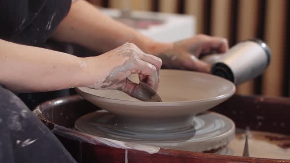 A Woman Heating the Clay Plate on the Pottery Wheel Using a Hairdryer and Removes Excess Clay From