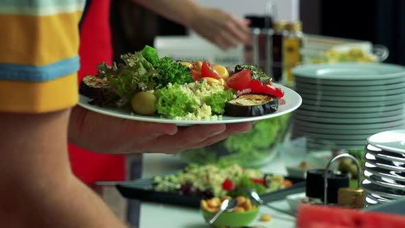 Man Puts Food on Plate From Table with Various Meals - Closeup