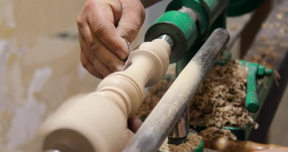 Closeup of person sanding wooden product using sandpaper on a lathe