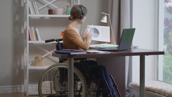 Portrait of Confident Caucasian Young Woman in Wheelchair Talking at Laptop Video Chat Pointing at
