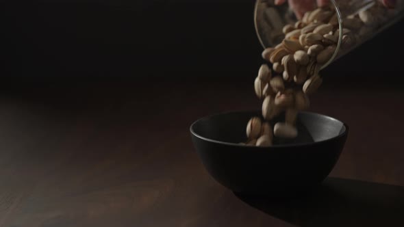 Slow Motion Roasted Pistachios Falling Into Black Bowl on Walnut Table