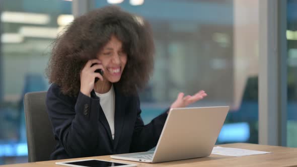 Angry African Businesswoman with Laptop Talking on Smartphone