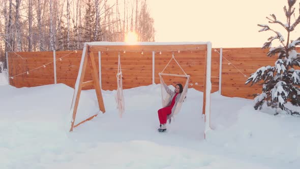 A Beautiful Girl on a Swing in a Country House on a Frosty Morning Meets the Sunrise in the Winter